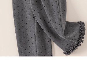 Detail view of grey knitted girls' pants with black heart prints and ruffled hem edges