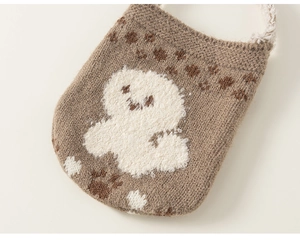 Detail of a brown knit pouch featuring a white plush dog pattern and cute paw prints