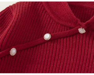 Detail of red ribbed knit sweater featuring elegant pearl buttons and side closure