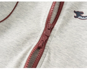 Détail d'un sweat à capuche gris avec double fermeture éclair bordeaux et logo
