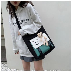 Detail of color-block canvas tote bag featuring smiley face print and plush bear pendant