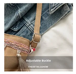 Close-up of beige canvas bag featuring ethnic embroidery, fringes, and silver metal buckle