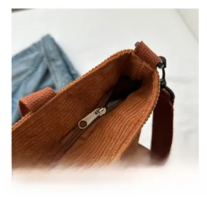 Detail of smooth metal zipper closure and wide strap on brown corduroy tote bag