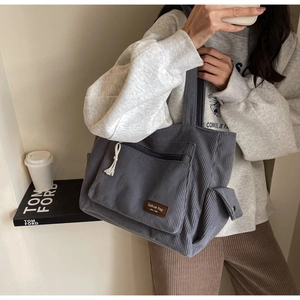 Detail view of grey corduroy tote bag showing zip pocket and brown leather patch
