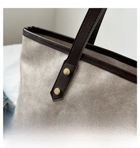 Close-up of the vintage gold rivets and brown leather stitching on a beige tote bag
