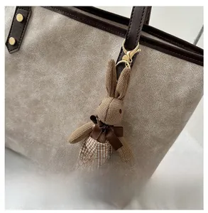 Detail of a brown knitted rabbit charm with metal clasp on a textured shoulder bag