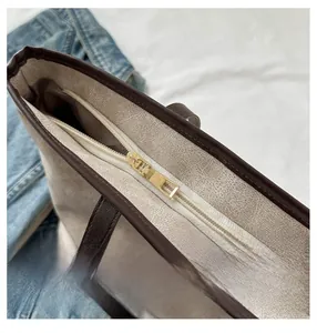 Close-up of golden smooth zipper closure on beige bucket bag with dark brown strap details