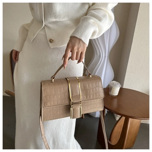 Detail view of khaki faux crocodile leather bag with gold buckle on model with white dress