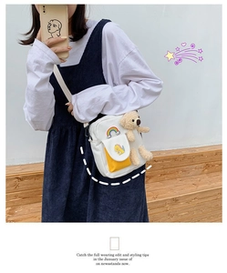 Détail du sac bandoulière en toile blanche avec poche jaune, écusson dinosaure et breloque ours