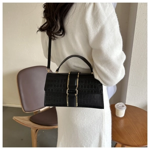 Close-up of black crocodile embossed leather handbag with elegant gold clasp on a model