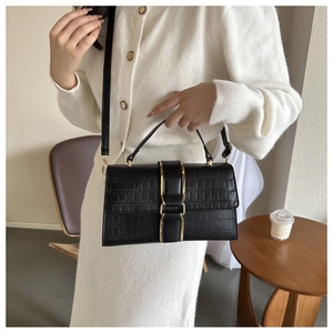 Close-up of black faux leather handbag with crocodile pattern and golden metal buckle