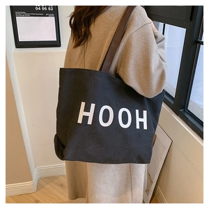 Détail du sac cabas en toile noire avec imprimé HOOH et anses en cuir marron sur l'épaule