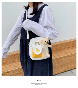 Détail du sac à bandoulière en toile blanche avec ours en peluche, écusson arc-en-ciel et poche
