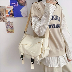 Detailed view of cream canvas messenger bag showing fashion tag and double buckle closure