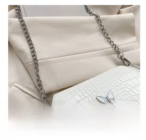 Detail shot of white croc-effect mini saddle bag with silver butterfly clasp and chain