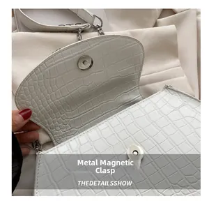 Macro shot of silver magnetic snap closure on white crocodile embossed leather bag