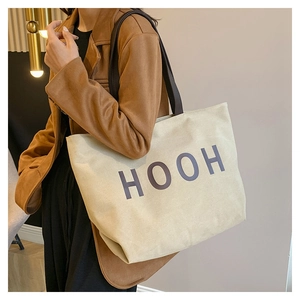Gros plan d'un sac cabas en toile beige avec imprimé HOOH et anses en cuir sur un modèle