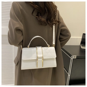 White crocodile pattern crossbody bag with gold buckle shown on a model in a brown suit