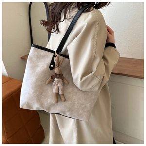 Detail view of beige tote bag with black handles and rabbit charm on trench coat