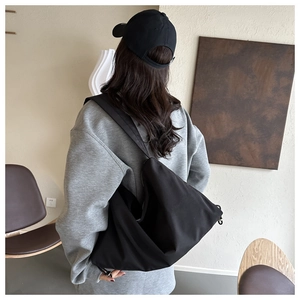 Vue latérale d'un grand sac bandoulière noir minimaliste en nylon porté par un mannequin