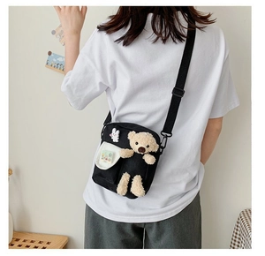 Détail du sac bandoulière en toile noire avec un ours en peluche et un badge lapin mignon