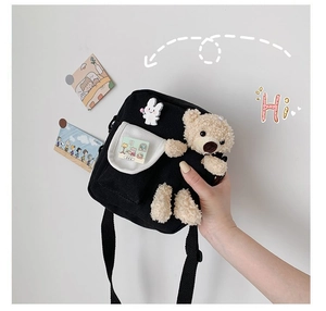 Détail du sac bandoulière en toile noire avec un ours en peluche 3D et une broche lapin