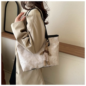 Detail of a large beige tote bag with black contrast trim and a cute rabbit pendant accessory