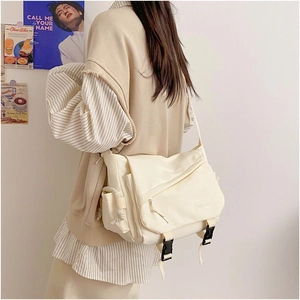 Close-up of cream canvas messenger bag showing buckle detail and adjustable strap on a model