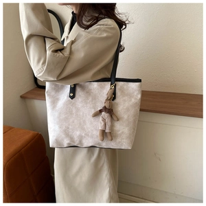 Detail of beige textured tote bag with black leather strap and rabbit charm accessory