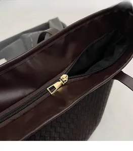 Close-up of smooth gold metal zipper and leather woven texture on a brown tote bag
