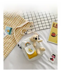 Détail d'un sac bandoulière en toile blanche avec poche jaune et peluche d'ours