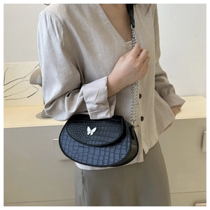 Detail of black croc-embossed saddle bag with silver butterfly clasp and chain strap