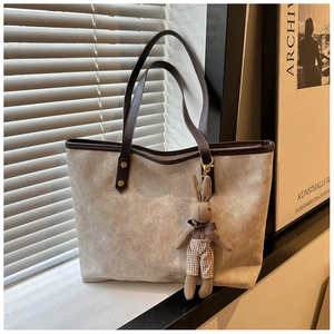 Detail of taupe suede tote bag with slim brown leather handles and cute bunny charm