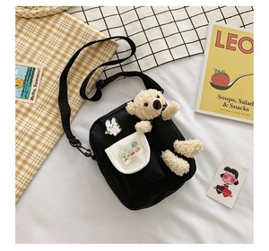 Détail d'un sac bandoulière en toile noire avec un ours en peluche 3D et badge de lapin