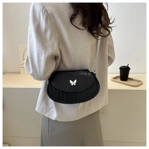 Detailed view of black crocodile pattern saddle bag with silver butterfly clasp and chain