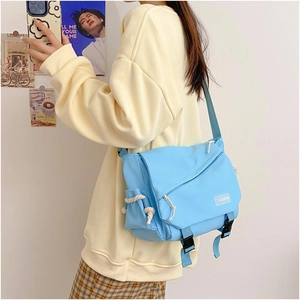 Blue canvas messenger bag with flap closure and white rope knot detail worn by a model
