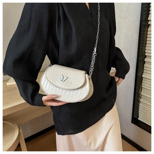 Detail of a creamy white crossbody bag with crocodile texture and silver butterfly ornament