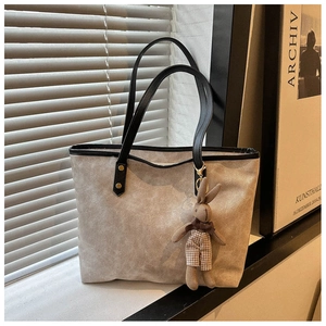 Detail of beige tote bag featuring black handles, gold rivets, and a plush bunny charm