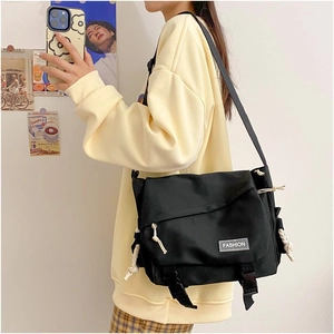 Close-up detail of black canvas messenger bag featuring fashion tag and dual buckle closure
