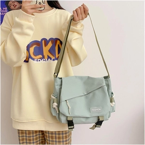 Detail of mint green canvas messenger bag featuring a fashion label and side pocket knot
