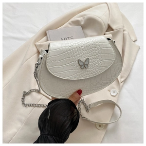 Close-up of cream crocodile pattern saddle bag with butterfly buckle and chain strap