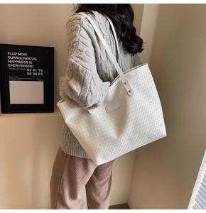 Detail view of white woven tote bag featuring golden studs and slim double shoulder straps