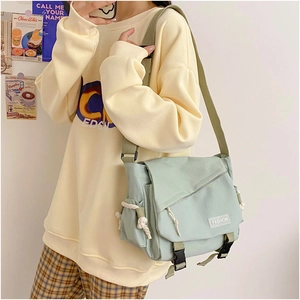 Close-up of mint green canvas messenger bag with double buckles and fashion label