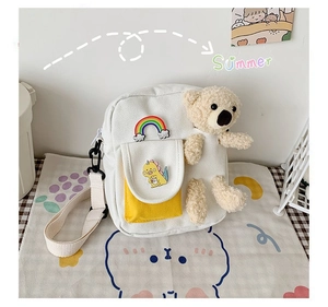Détail du sac bandoulière en toile blanche avec ours en peluche et poche jaune à dessin