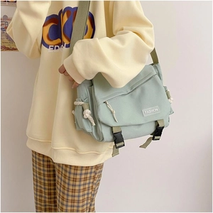 Close-up of mint green canvas messenger bag with double buckles on a yellow sweatshirt
