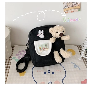 Détail d'un sac bandoulière en toile noire avec ours en peluche et écusson lapin