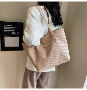 Detail of woven beige tote bag featuring thin shoulder straps and metallic gold rivets