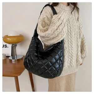 Detail of black quilted hobo bag with wide shoulder strap worn over a knit sweater