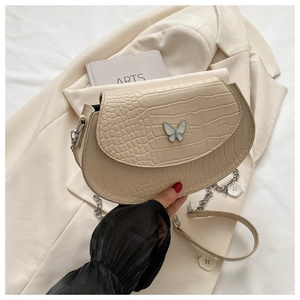Close-up of cream saddle bag featuring crocodile texture and butterfly metal clasp