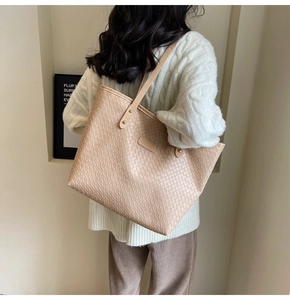 Model wearing a large beige woven leather tote bag with elegant metallic rivets